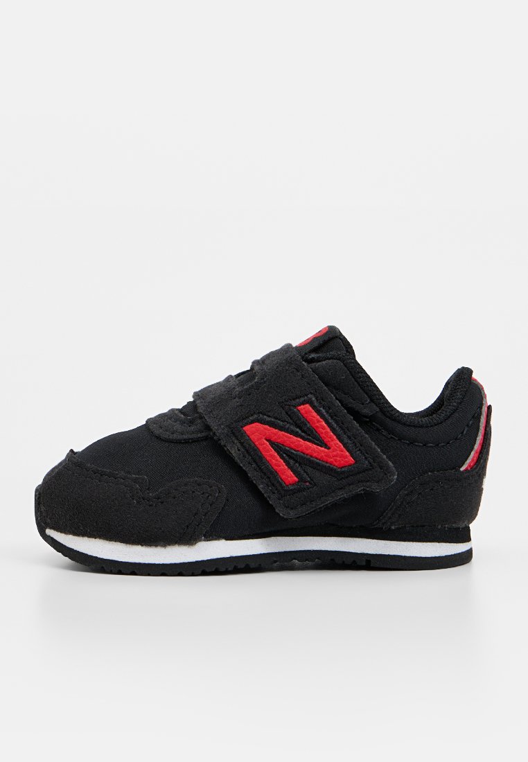 Baskets en tissu noir avec des accents rouges, bande Velcro, surface texturée, bout arrondi et semelle en caoutchouc blanc. Présente le logo 'N' en évidence.