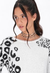 Weißer, flauschiger Pullover mit einem schwarzen Leopardenmuster. Kombiniert mit einer mehrsträngigen Perlen-Choker-Halskette in Schwarz und Weiß.