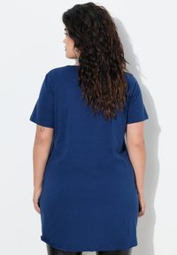 Maglietta blu oversize con maniche corte, scollo rotondo e una texture liscia, che si estende fino a metà coscia. Presenta un orlo incurvato.