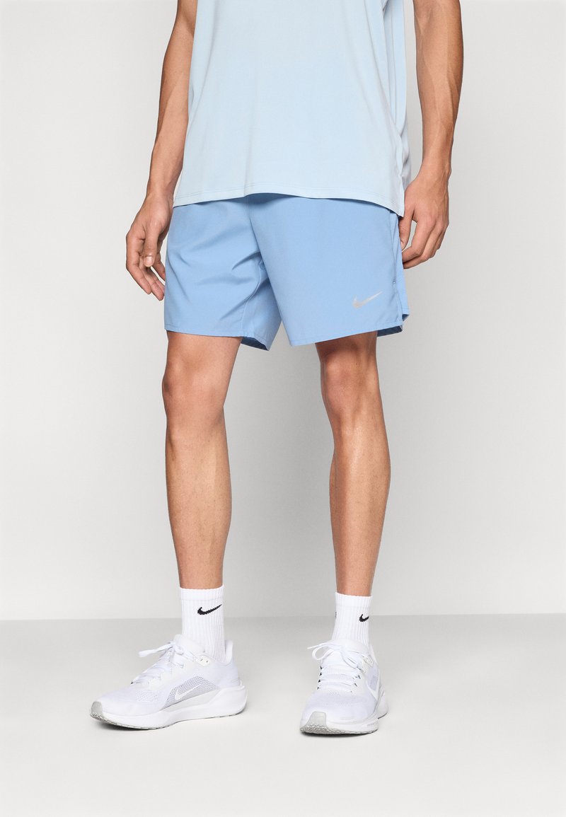 Ανοιχτά μπλε αθλητικά σορτς με ομαλή υφή και λογότυπο της Nike σε ασημί χρώμα. Συνδυάζονται με άσπρα αθλητικά παπούτσια και κάλτσες αστραγάλου.