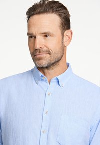 Vaaleansininen nappipaita, joka on valmistettu tekstuurista kankaasta. Paidassa on tasku vasemmalla puolella ja vaaleat napit.