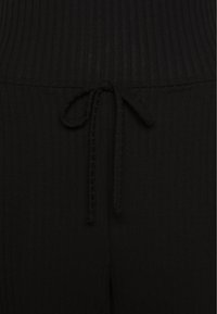 Czarne dresowe spodnie z żebrowanej tkaniny o miękkiej fakturze, z kieszenią na sznurku i luźnym krojem.