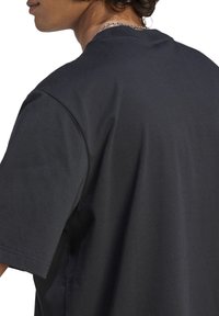 Czarny bawełniany t-shirt o luźnym kroju, z krótkimi rękawami i zaokrąglonym dekoltem. Gładka faktura, minimalne detale na plecach.