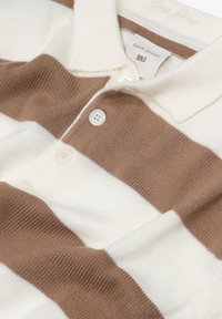 Gestreiftes Polohemd in Braun und Creme, mit gestrickter Textur, drei Knöpfen und einem Kragen, versehen mit einem Etikett mit der Aufschrift "DAN JOHN."
