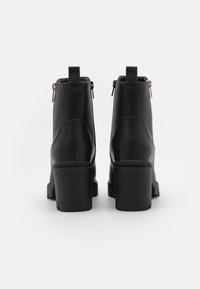 Botas negras de cuero hasta el tobillo con un tacón grueso, que cuentan con un cierre de cremallera en el lateral y una lengüeta en la parte trasera. Textura suave con un detalle mínimo.