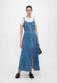 Denim-maksi mekko, jossa on edessä vetoketju, säädettävät hihnat ja sivuhaalari. Yhdistetty valkoisen tekstuuripaitan päälle, mustat liukuhalkaset kengät.