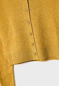 Senfgelber Strickcardigan mit fünf Knöpfen und geripptem Saumdetail auf einer flachen Fläche.