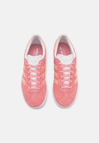 Ein Paar rosa Adidas Wildleder-Sneaker mit pfirsichfarbenen Streifen und weißen Sohlen, von oben auf einem weißen Hintergrund betrachtet.