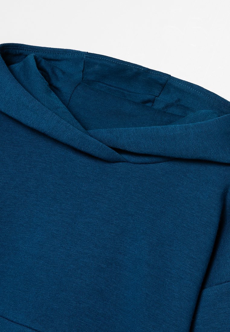 Haut à capuche en coton bleu avec une texture lisse, présentant un col arrondi et une coupe décontractée. Le tissu semble doux et élastique.