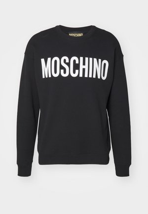 Juodas megztinis, pagamintas iš minkštos medžiagos, su baltu "MOSCHINO" logotipu priekyje, apvalia dekoltė ir struktūruotais rankogaliais bei apačia.