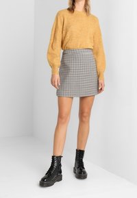 Sweter w kolorze rdzy, dopasowana czarno-biała minispódniczka w kratę oraz czarne, wiązane buty typu combat z masywną podeszwą.