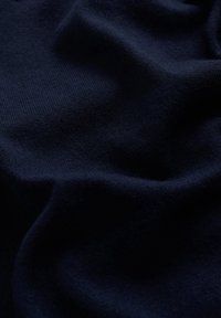 Tmavě modrá látka má jemnou texturu s matným povrchem, která se vyznačuje hladkým povrchem a jemným vzorem pletení.