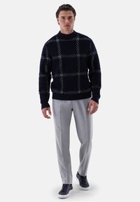 Marineblauer Strickpullover im Schachbrettmuster, kombiniert mit hellgrauen, maßgeschneiderten Hosen und dunklen Sneakers. Lockerer Schnitt, gerippte Bündchen und Ausschnitt.