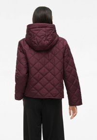Burgundy quilted jacket with a hood, featuring a diamond pattern, elastic cuffs, and a boxy cut, providing a warm and contemporary look.