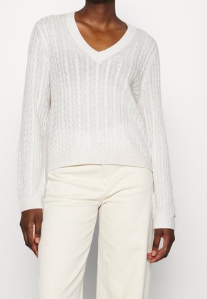 Pull en maille côtelée beige clair avec un col en V et des manches longues, arborant un motif texturé et un ourlet côtelé.