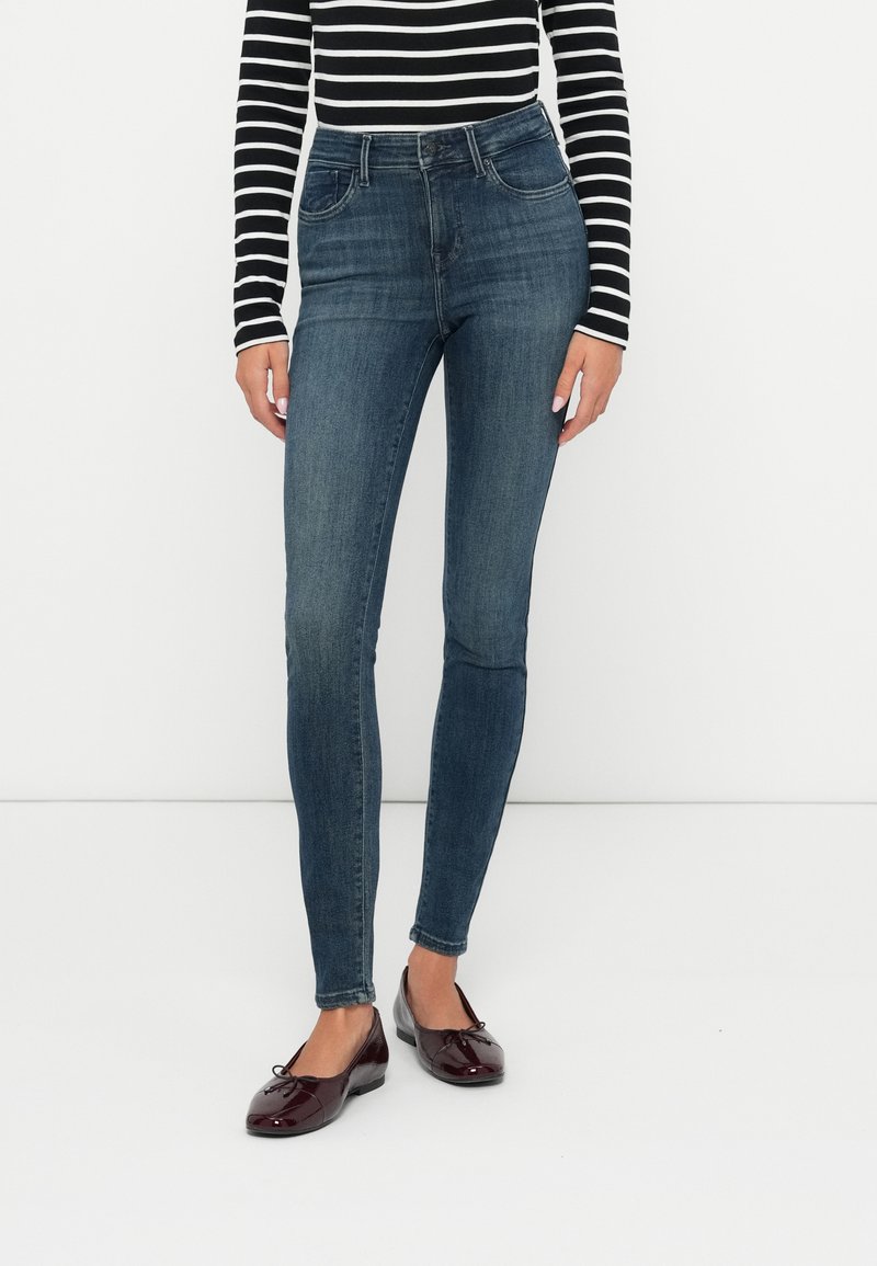 Jeans de mezclilla oscuros de talle alto con un corte slim, que cuentan con bolsillos frontales y un diseño cl�ásico de cinco bolsillos, combinados con zapatos planos burdeos.