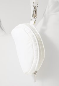 White padded crossbody bag with two zip compartments, featuring silver hardware and a detachable strap. Smooth texture and rounded shape.