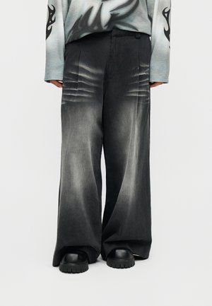 Czarne spodnie z szerokimi nogawkami, z wyblakłymi zagnieceniami wokół bioder, noszone z masywnymi czarnymi butami i szarą koszulą z długim rękawem z czarnymi płomieniami na rękawach.