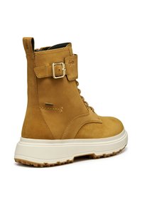 Stivale alla caviglia in pelle color tan con suola chunky bianca, cinturino laterale con fibbia, lacci e battistrada testurizzato per l'uso all'aperto.