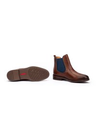 Brown leather Chelsea boots with navy elastic side panels, one boot upright, one boot lying on its sole showing tread pattern.