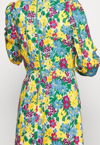 Blommig klänning med en livlig blandning av gult, blått, grönt och rosa, med puffärmar och en dragkedja i mitten.