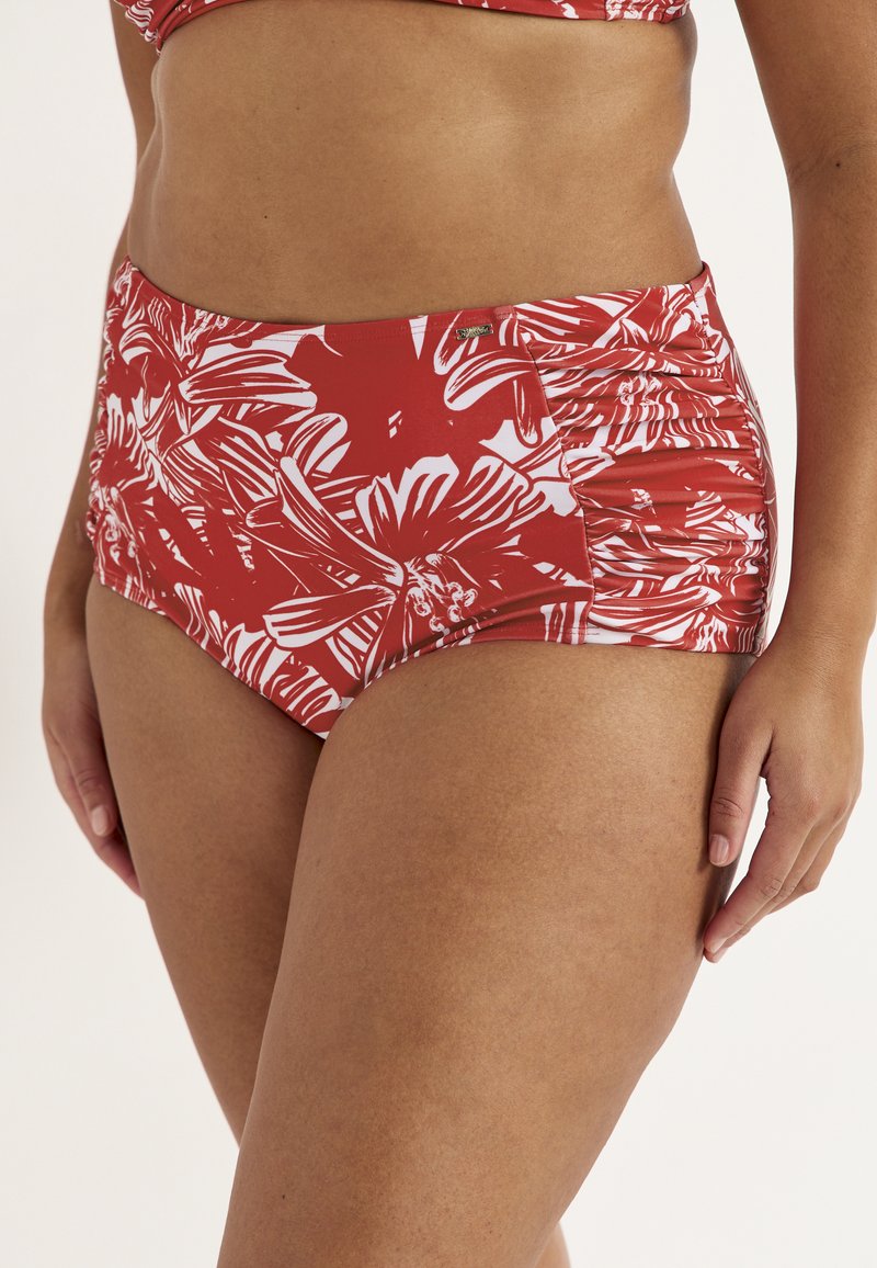 Røde og hvide blomstrede bikinitrusser med høj talje og rynkede sider, båret af en person med mellemtonet hud, der står mod en ensfarvet baggrund.
