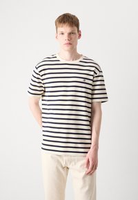 Striped t-shirt in cream and navy, featuring a textured fabric, round neck, short sleeves, and a small logo on the chest.