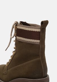 Braune Wildleder-Ankle-Boots mit einem strukturierten Stoffbund, der ein gestreiftes Muster aufweist. Schnürdesign mit Metallösen und einer Zuglasche.