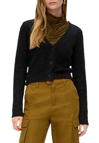 Cardigan noir texturé avec un col en V et une fermeture à boutons, associé à un col roulé côtelé vert foncé et un pantalon cargo olive.