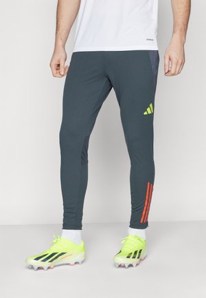 Grijze sportlegging met donkergrijze panels, oranje zijkanten en een strakke pasvorm. Gecombineerd met felgele voetbalschoenen met zwarte accenten.