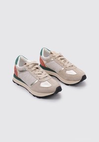 Sneaker in suede beige con dettagli metallici, dotati di un tassello verde sul tallone e pannelli laterali corallo; superficie texturizzata e suola in gomma nera.