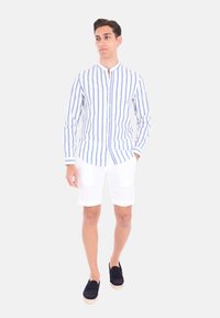 Camicia a maniche lunghe con bottoni, a righe orizzontali blu e bianche, abbinata a pantaloni corti bianchi e scarpe slip-on blu navy.