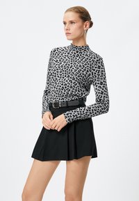 Top a maniche lunghe grigio con stampa leopardata nera, abbinato a una gonna nera e una cintura nera, caratterizzato da un design aderente e colletto alto.
