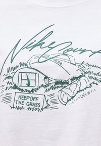 Raquette de tennis, balle et serviette roulée sur l'herbe avec un panneau « KEEP OFF THE GRASS » et le texte « Nike Court » au-dessus.