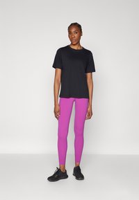 Schwarzes T-Shirt mit kurzen Ärmeln, kombiniert mit figurbetonten, leuchtend pinken Leggings und schwarzen Sportschuhen. Einfaches Design und glatte Textur.