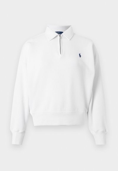 Sudadera polo blanca hecha de tela suave, con cierre de cremallera de cuarto, mangas largas y un pequeño logo azul marino en el pecho.