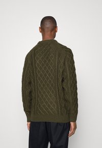 Suéter de punto en verde oliva oscuro con un patrón de cable de textura. Presenta mangas largas, un cuello y un dobladillo acanalados.