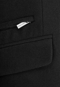 Czarna kurtka z mieszanki wełny, z zapinaną na zamek kieszenią i metką. Materiał ma miękką teksturę i gładkie wykończenie.