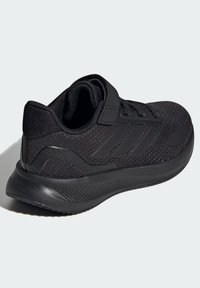Chaussure de sport noire avec une tige en tissu texturé, des détails en mesh, un col rembourré, une sangle Velcro et une semelle en caoutchouc arborant un motif rayé.