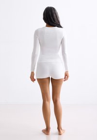 White long-sleeve top and matching shorts, made of smooth, stretchy fabric. Form-fitting design with minimal seams and a clean silhouette.