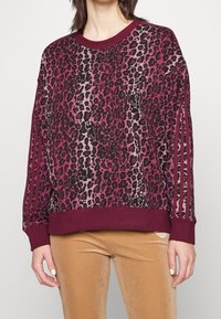Sweter w cętki w odcieniach burgundu i czerni, z prążkowanym dekoltem oraz trzema paskami na rękawach. Miękka tekstura materiału.