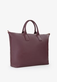 Borsa tote in pelle bordeaux con una texture liscia, doppio manico, chiusura con zip e forma rettangolare. Presenta elementi di design minimalisti.
