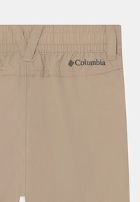 Béžové kalhoty Columbia s elastickým pasem a prošívanými detaily. Na pase se nachází černé logo. Lehce materiál.