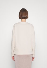 Krémová mikina s kulatým výstřihem a dlouhými rukávy, hladká textura, doplněná lesklou růžovou sukní.