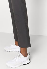 Grijze cropped broeken met een zijlusdetail, gecombineerd met witte mesh sneakers met zwarte zolen en veters voor een veilige sluiting.