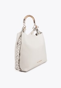 Štýlová off-white kabelka s opleteným bočným dielom a zakrivenou zlatou rukoväťou. Názov značky je nenápadne vyrazený na prednej strane.