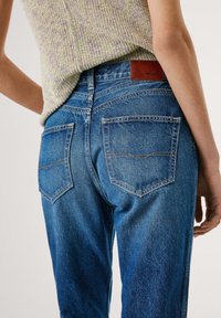 Blaue Denim-Jeans mit hoher Taille, geradem Bein und zwei Gesäßtaschen. Verfügt über kontrastierende Nähte und ein braunes Leder-Brandpatch.