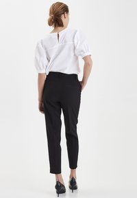 Blusa bianca con maniche a sbuffo e dettaglio a chiave sulla schiena, abbinata a pantaloni neri a gamba affusolata e tacchi a punta neri.