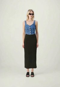 Top court en denim avec des boutons, associé à une longue jupe noire côtelée. La mannequin porte des sandales plates noires et des lunettes de soleil rectangulaires.