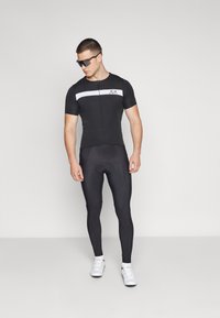 Radanzug mit kurzen Ärmeln, schwarzem Stoff, weißem Horizontalstreifen, Reißverschluss vorne, figurbetontem Design, kombiniert mit schwarzen Leggings und weißen Schuhen.
